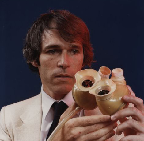 A portrait of Robert Jarvik holding an artificial heart in front of his face. 