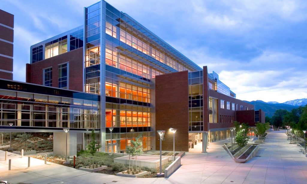 The Eccles Health Sciences Education Building with all of its lights on against a partly cloudy, blue hour sky